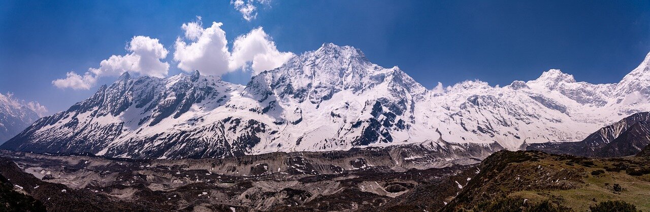 A large group of climbers in colorful gear celebrates at the summit of Mount Everest, with a breathtaking view of snowcapped peaks and a clear blue sky in the background.