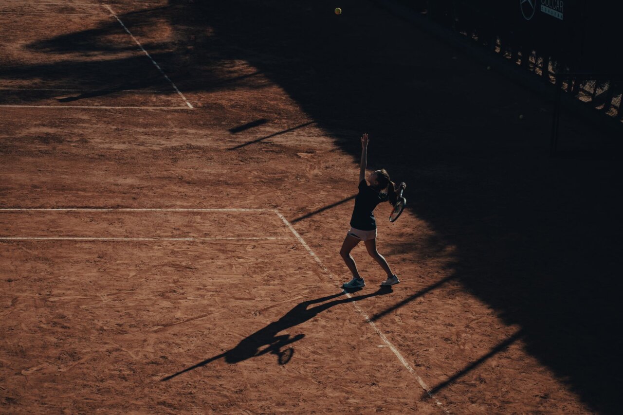 Naomi Osaka delivering a powerful serve during a night match, highlighting the intensity and skill present in women's tennis