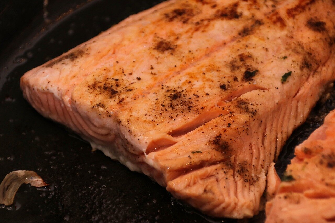 A chef skillfully broils salmon fillets in a kitchen, with bright flames visible from the broiler and fresh herbs scattered on the countertop.