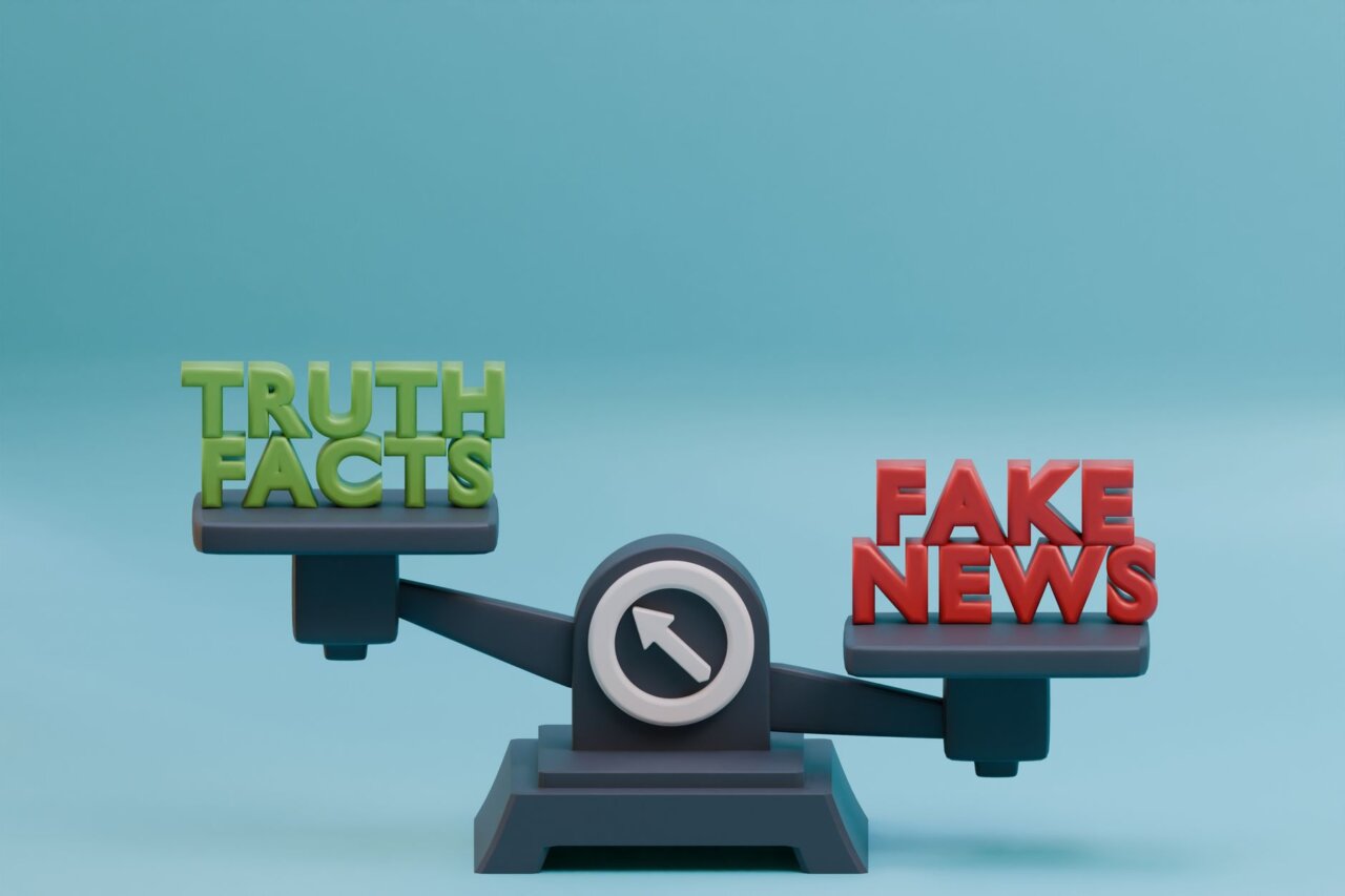 Tim Heidecker stands on stage with a microphone, flanked by The Onion team, as they announce their campaign against InfoWars during a live event filled with an engaged audience.